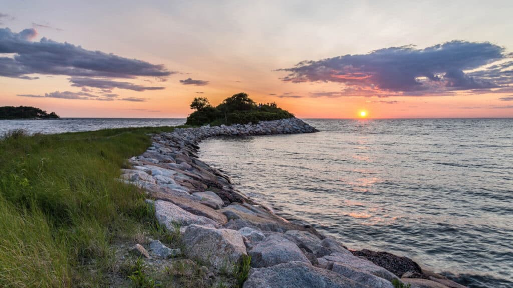A rocky hillside leading to the ocean at sunset.
