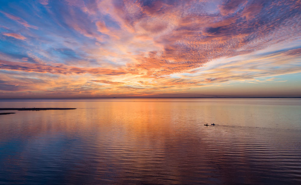 Still ocean with two people kayaking on it at sunset.