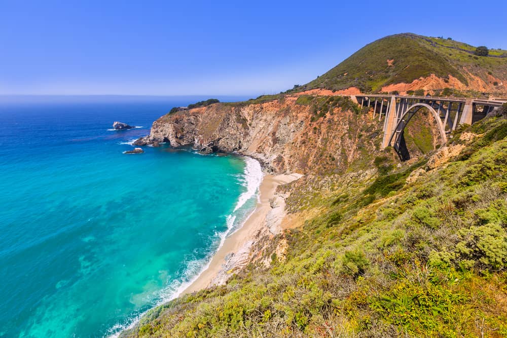 A large cliffside overlooking a bright green and blue beach.