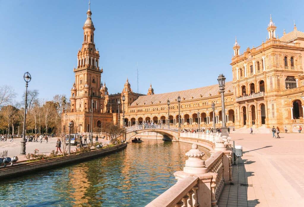 A small river cutting through a city with a large palace like building to the right.