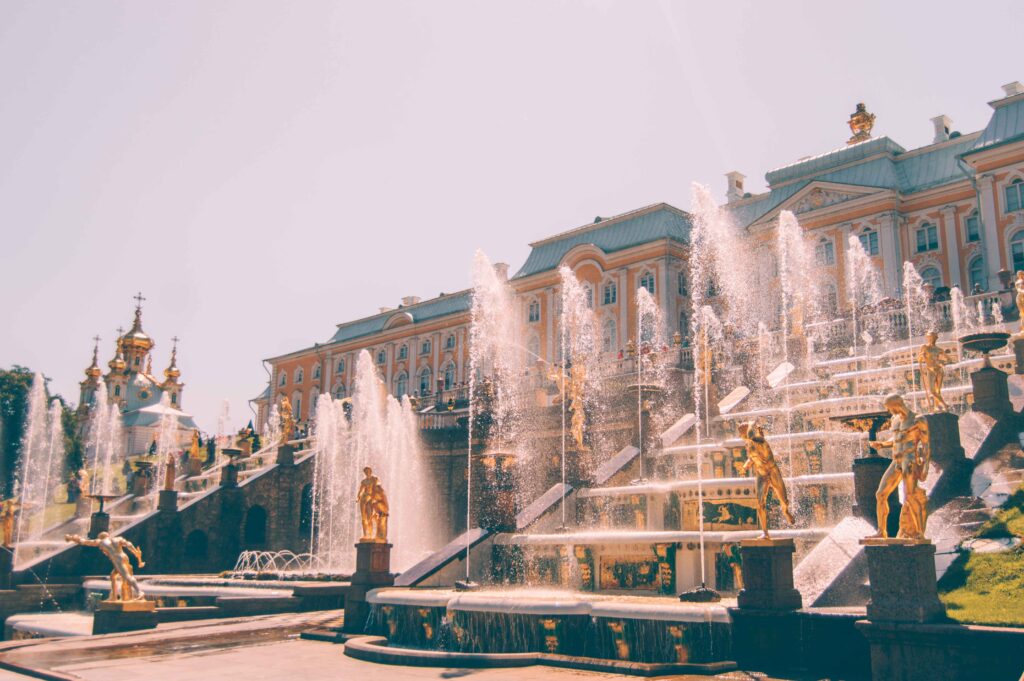 A large water feature with various gold statues throughout it in front of a large palace.