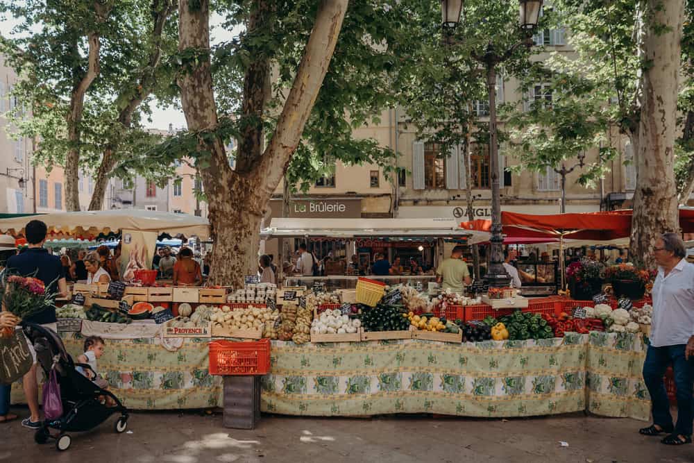 People shopping at a farmer's market on a busy street in France.
